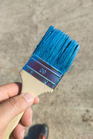 Painting a wooden fence with acrylic paint. House painter shows his flat brush beaver blue...