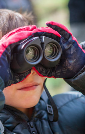 Child boy holds binoculars in nature. He is wearing gloves and a camouflage anorakの写真素材