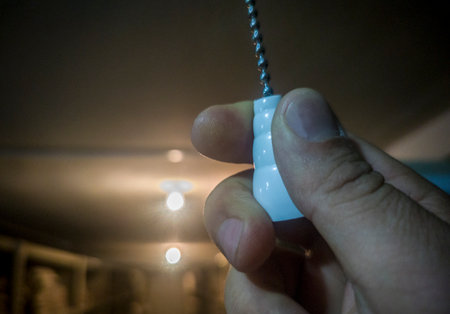 Hand pulling a light porcelain chain light switch attached to the ceiling. Selective focus