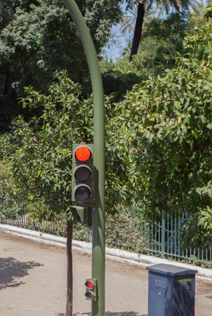 Red traffic light with control box beside. Signaling device positioned close to public park