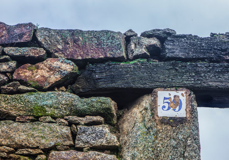 Rustic house number 59 placed on the wooden lintel of a ruined stone houseの写真素材