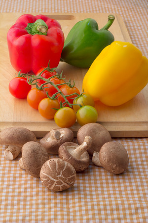 fresh tomato and mushroom with sweet peppers on wooden plate with brown fabric backgroundの写真素材