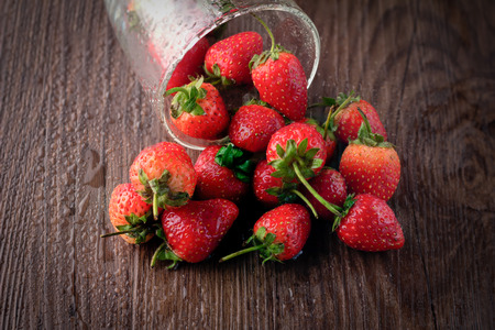 Small glass bowl filled with succulent juicy fresh ripe red strawberries on an old wooden textured table topの写真素材