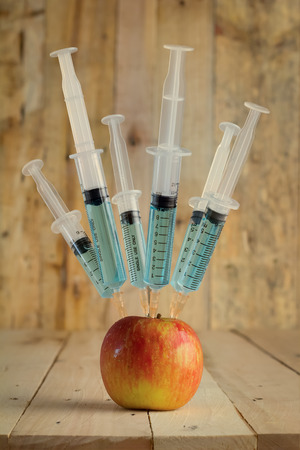 Injection into red apple -  Concept for Genetically modified fruit and syringe with colorful chemical GMO foodの写真素材