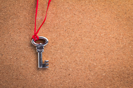 an old rustic key with red ribbon on cork board texture backgroundの写真素材