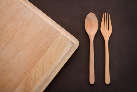 wooden spoon and fork on cutting pad on dark brown background  with copy space for your textの写真素材