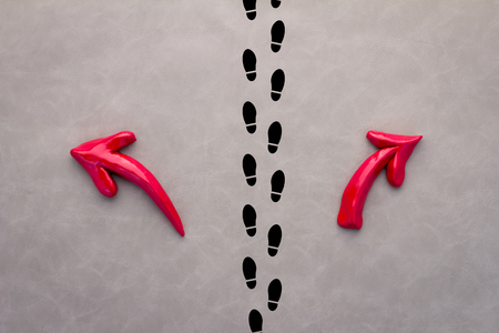 A pair of feet standing on a tarmac road with red arrow  in two different directions for the concept of making decision at the crossroad.の写真素材