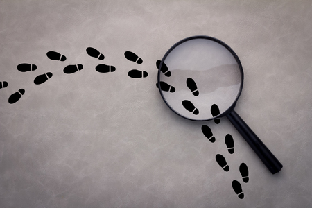 Magnifying glass over footsteps on grey backgroundの写真素材