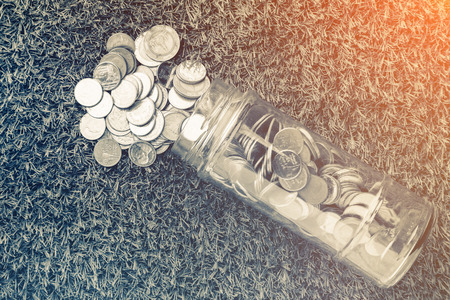 Coins spilling out of a glass bottle with filter effect retro vintage style business saving concept