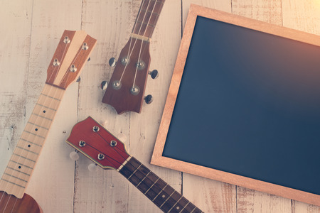 empty chalkboard and ukuleles on the white vintage wooden terrace with vintage color filter toneの写真素材