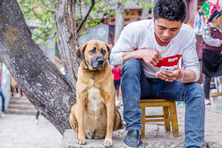 Lijiang, China - April 12, 2016: man is sitting with dog on the street in Lijiang, Chinaのeditorial素材