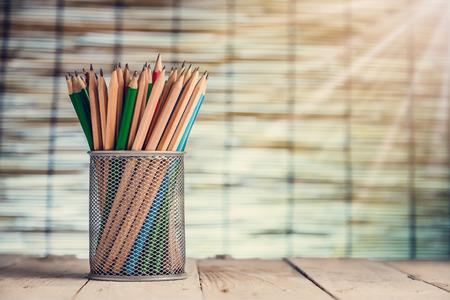 Group of pens and wooden pencils in metal vase on wooden floorの写真素材