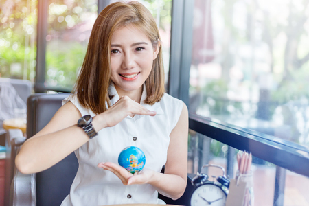 beautiful asian girl holding a globe  in her hand in cofffee shop with nature and light flare effect safe world conceptの写真素材