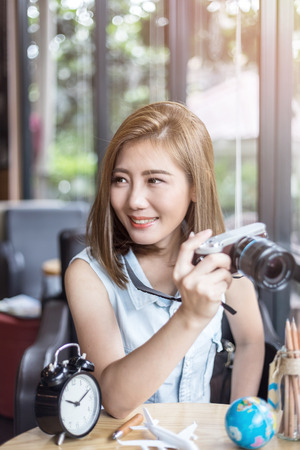 beautiful asia girl with camera with alarm clock plane toy globe in cafe with travel concept light flare effectの写真素材