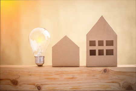 paper houses stands over a wooden background with glow light bulb house ideas conceptの写真素材