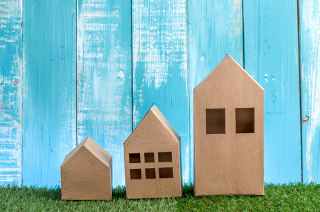 model of cardboard house on green grass floor and wooden background. house building, loan, real estate or buying a new home concept.の写真素材