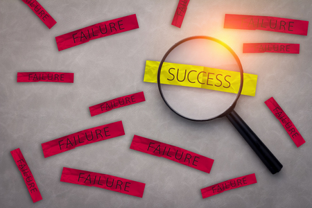 BUSINESS SUCCESS CONCEPT WITH SUCCESS AND FAILURE ON A PAPER NOTE WITH MAGNIFYING GLASS ON GREY LEATHER BACKGROUND AND FREE COPY SPACE FOR YOUR CREATIVITY IDEAS CONCEPTの写真素材
