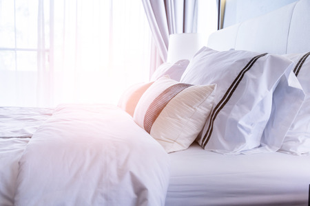 Bed maid-up with clean white pillows and bed sheets in beauty room. Close-up. Lens flair in...