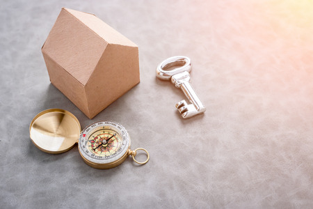 house in brown recycled paper on grey leather background  with silver key and compass with free copy space  for your text ideas house conceptの写真素材