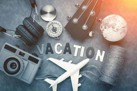 vacation ideas concept with travel stuffs camera ukulele headphone,plane,globe,compass with wwoden text word on grey leather background with light flare effectの写真素材