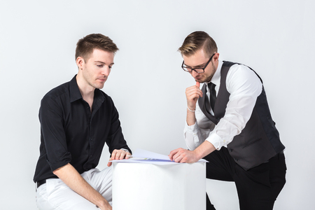 Two businessmen discussing tasks sitting and looking at business graph chart with white baclgroundの写真素材
