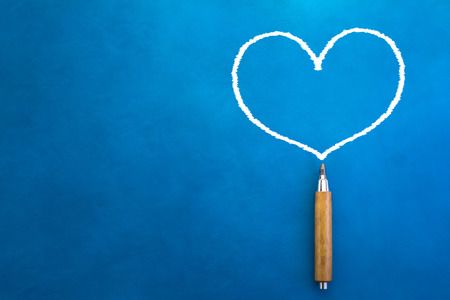 drawing of white heart shape with wooden pencil on blue background with free copyspaceの写真素材