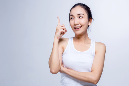 Portrait of a beauty asian smiling girl pointing finger up at copyspace isolated on a gray backgroundの写真素材