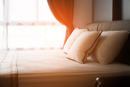 Bed maid-up with clean white pillows and bed sheets in beauty room. Close-up. Lens flair in sunlight.の写真素材