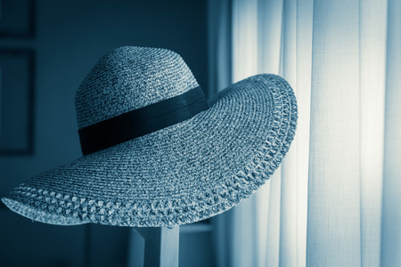 Women's Wide Brim Straw Hat hand on wood stand with light from white window curtain in daytimeの写真素材