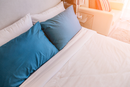 Bed maid-up with clean white pillows and bed sheets in beauty room. Close-up. Lens flair in sunlight.の写真素材