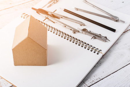 house deisgn concept with house paper cardboard and drawing tool on notebook and vintage wood backgroundの写真素材