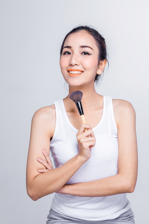 Beauty makeup asian woman smiling closeup. Beautiful young woman applying foundation powder or blush with makeup brush. Isolated on white background.の写真素材