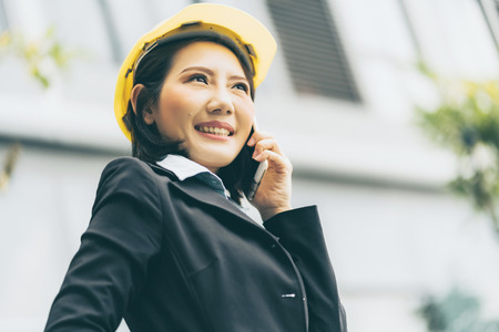 smart asian engineer with yellow helmet contact partner with smartphone  building background...