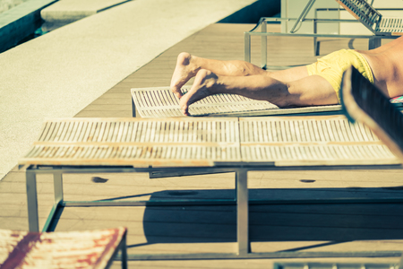 closed up man caucasian sun bath on wooden bench next to swimming pool deck with happiness weekendの写真素材