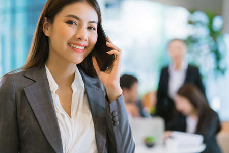 close up smart attractive asian business female smile hand hold smartphone with modern office backgroundの写真素材