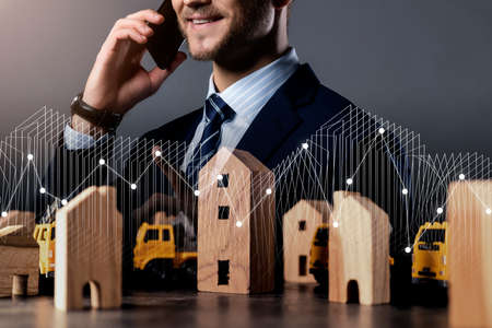 caucasian Successful businessman hand hold smartphone with house model and financial graph chart...