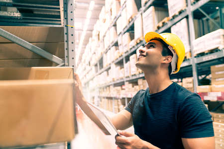 Smart Indian engineer man wearing safety helmet doing stock tick check and cardboard stock product...