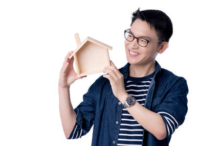 business insurance communication ideas concept with asian attractive male casual tshirt hand hold wooden house model box smile and happiness hand gesture pose present point show joyful momentの写真素材