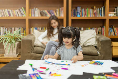 beautiful attractive caucasian child  girl doing painting with  mother read book behind house family...