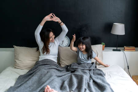 happy morning moment family single mom with girl daughter wake up and stretch together on bed