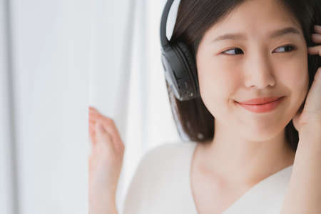 relex and peaceful asian woman enjoy weekend with music headphone morning sunlight near window home...