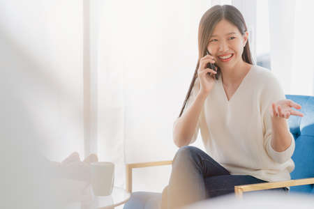 beautiful asian woman communication with friend in happiness mood morning weekend home backgroundの写真素材
