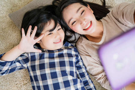 happy Asian Family mother  and daughter making a selfie photo while use  in living room home background.の写真素材