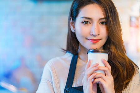 beautiful attractive asian cafe shop owner smile with happiness and joyful with coffee cup apron cafe  backgroundの写真素材