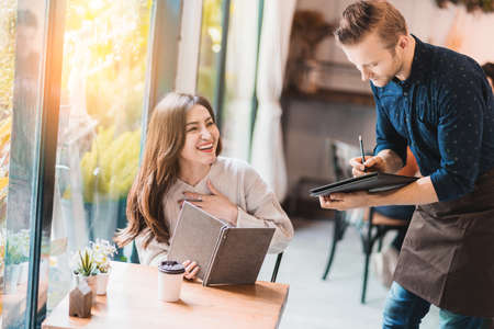 attractive asian woman order something with waiter in cafe restaurantの写真素材