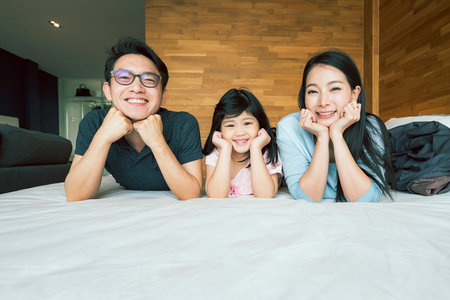 happiness joyful asian family mom dad daughter laydown together with fun play kiss on bed portrait of asian family people home backgroundの写真素材