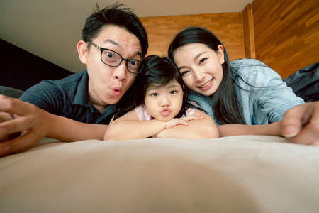 happiness joyful asian family mom dad daughter laydown together with fun play kiss on bed portrait of asian family people home backgroundの写真素材