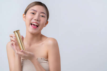 skincare and makeup concept beautiful asian female woman with healthy facial skin close up portrait studio shot hand hold serum pr cream package with happiness and joyfulの写真素材