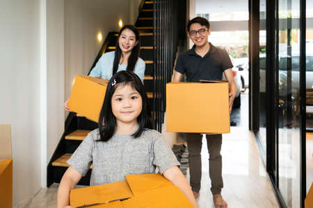 happiness asian family mom dad daughter moving in new house hand carry box of stuff with exited and...