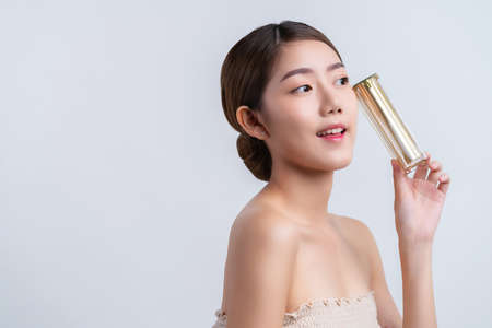 skincare and makeup concept beautiful asian female woman with healthy facial skin close up portrait studio shot hand hold serum pr cream package with happiness and joyfulの写真素材